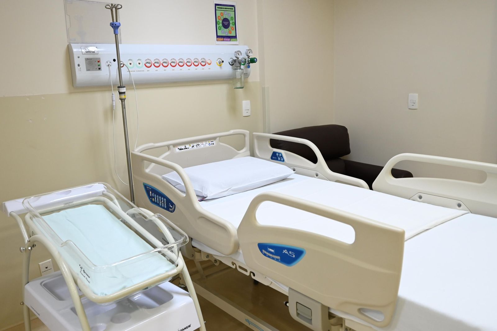 Na imagem há um leito de hospital com uma cama e um equipamento instalado na parede.
